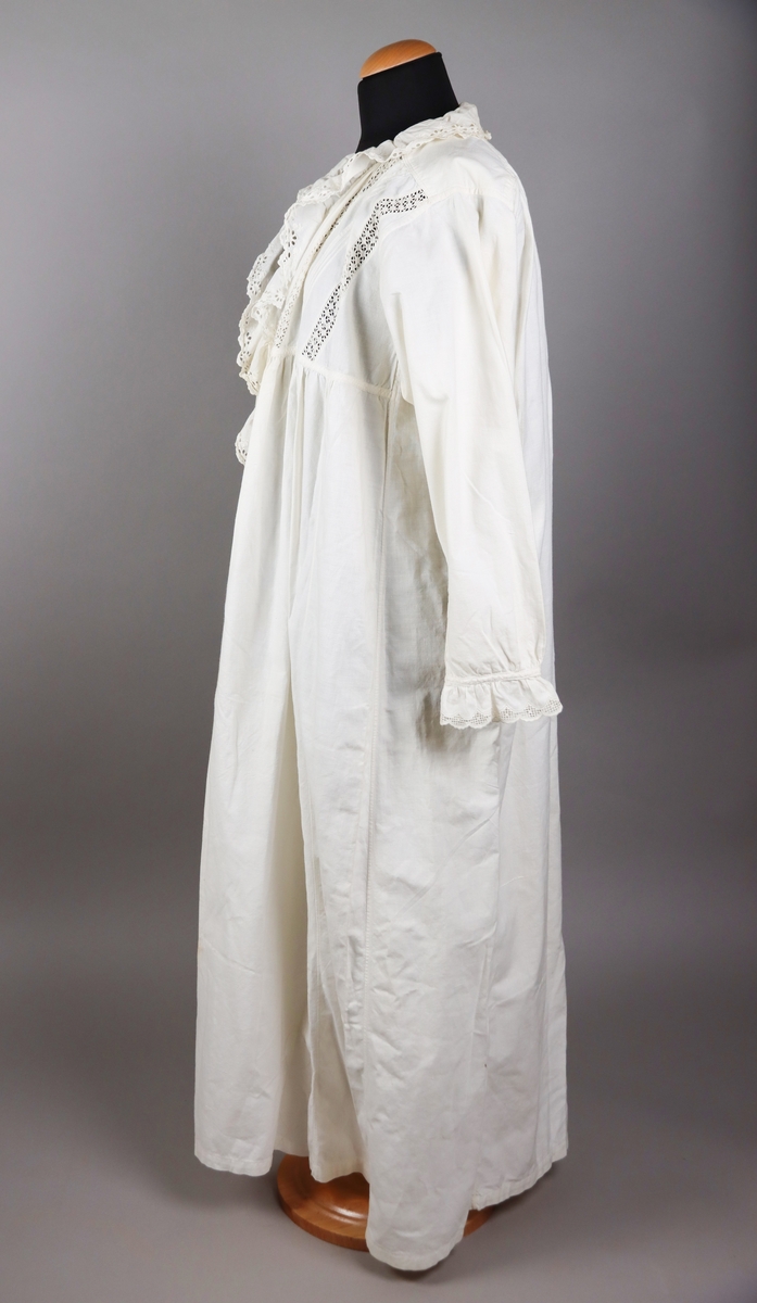 Nattsärk av vit bomull med brodyr. Långa ärmar. Ryggstyckets vidd rynkad mot axelpartiet på ryggen. Djupt ringad på framsidan. Ringningen kantad med bred broderad spets. Dekor av knypplade spetsband som infällts i framstycket över bröstet.
