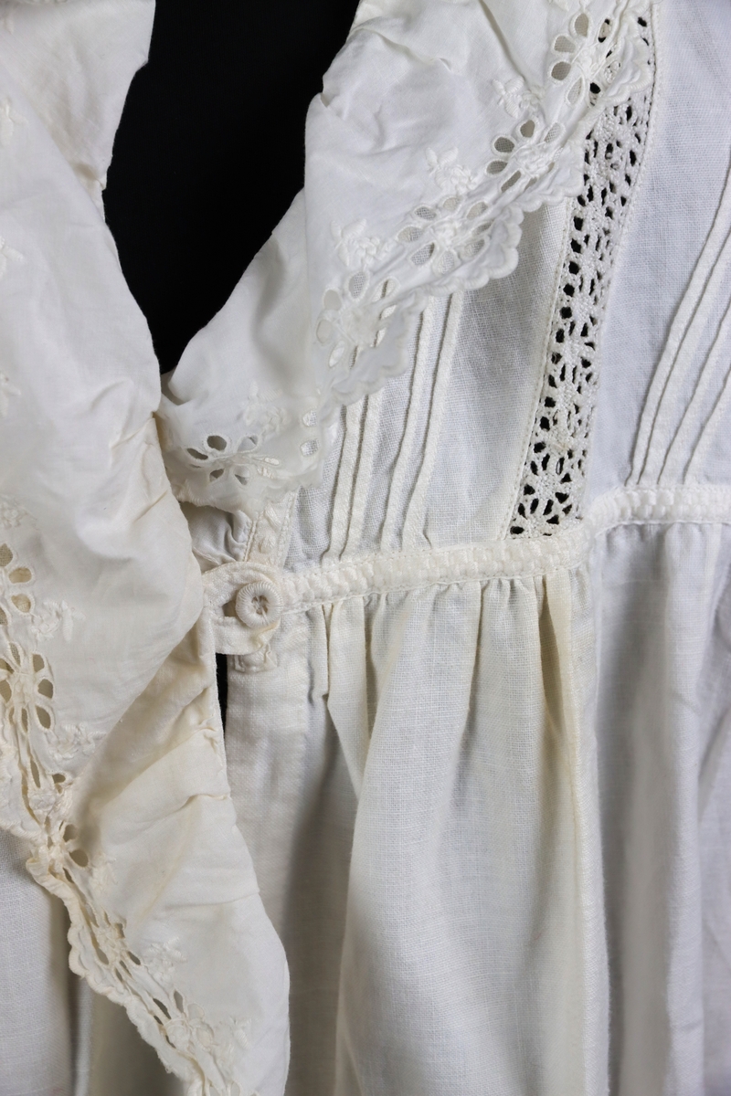 Nattsärk av vit bomull med brodyr. Långa ärmar. Ryggstyckets vidd rynkad mot axelpartiet på ryggen. Djupt ringad på framsidan. Ringningen kantad med bred broderad spets. Dekor av knypplade spetsband som infällts i framstycket över bröstet.