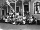 Gruppbild med ett stort antal barn vid en veranda till ett stort trähus, troligen en skola med skolbarn.