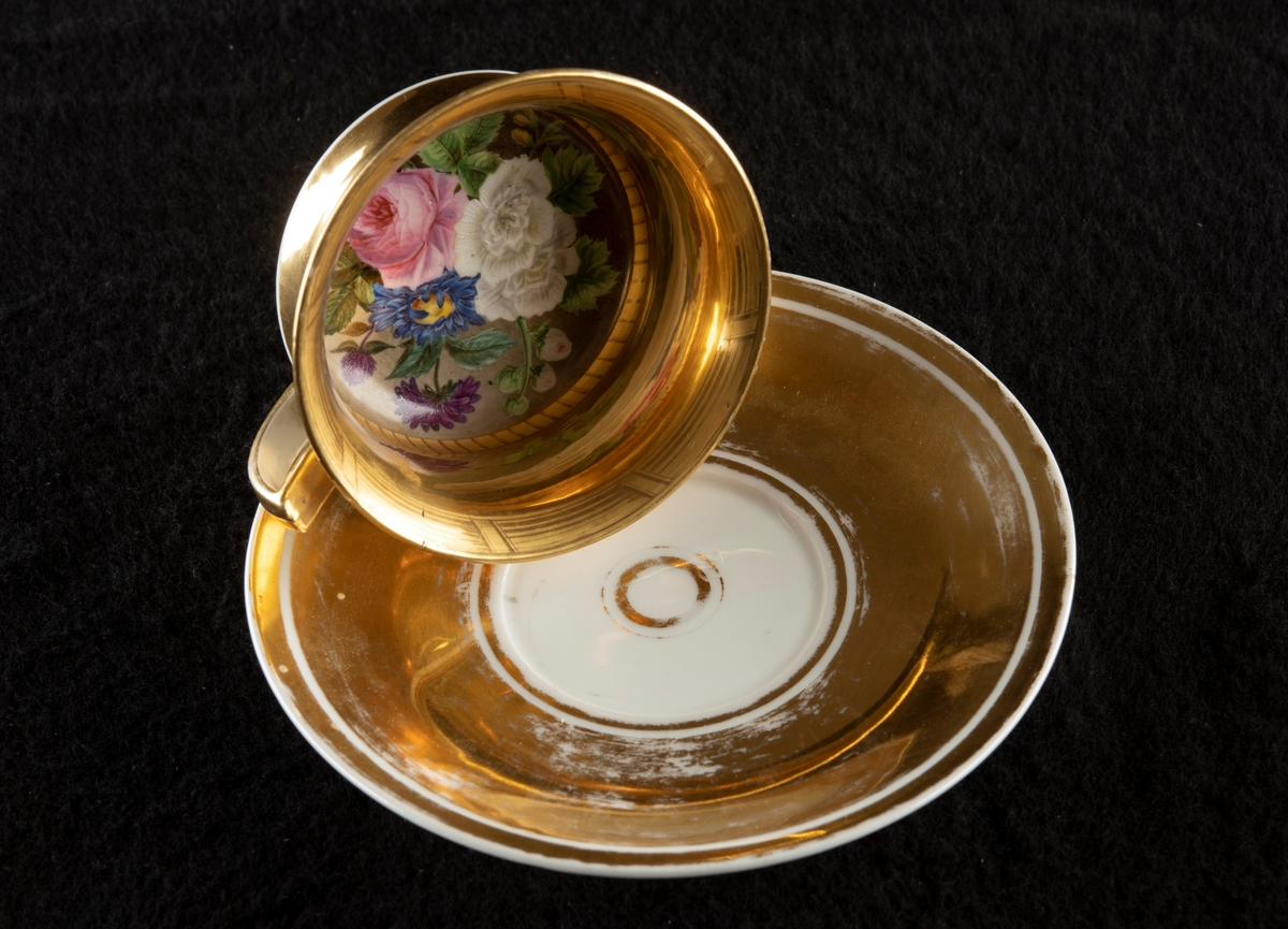 1: Kopp med öra, rund fotring, insvängd mitt, utåtvikt mynningskant. Förgylld, handmålad dekor, blommotiv i vitt, rosa, blått, gult, grönt och rött. 2: Fatets ovansida förgyllt, vita dekorränder. Höjd 22 mm, diameter 152 mm.