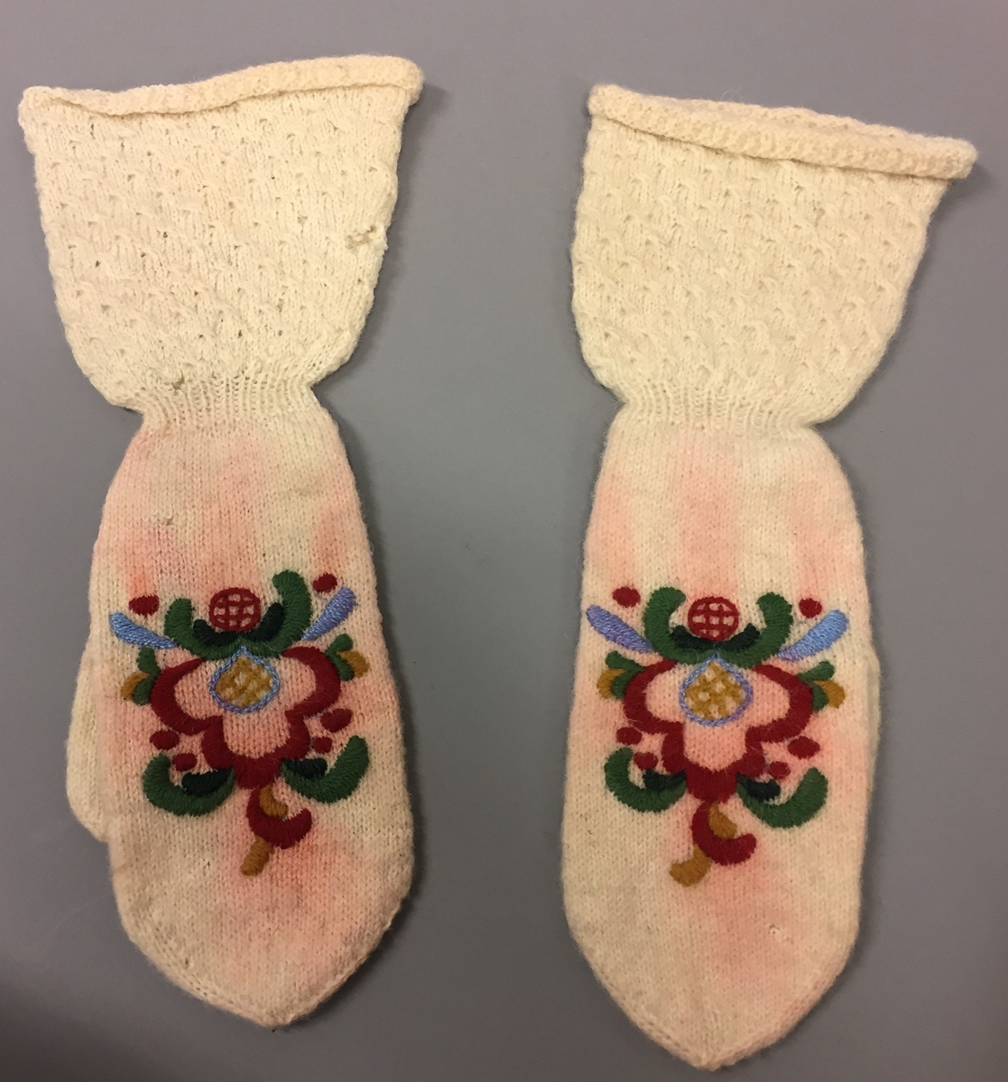 Heimestrikka vottar i glattstrikk med rosesaum. Vottane har mønsterstrikk på velet. Ikkje tommelkile. Strikka av heimespunne garn. Plattsaum i sterke fargar,saumen har farga noko av.