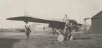 En man håller upp flygplan Thulin B i stjärtfenan. På ett flygfält cirka 1915-1918.