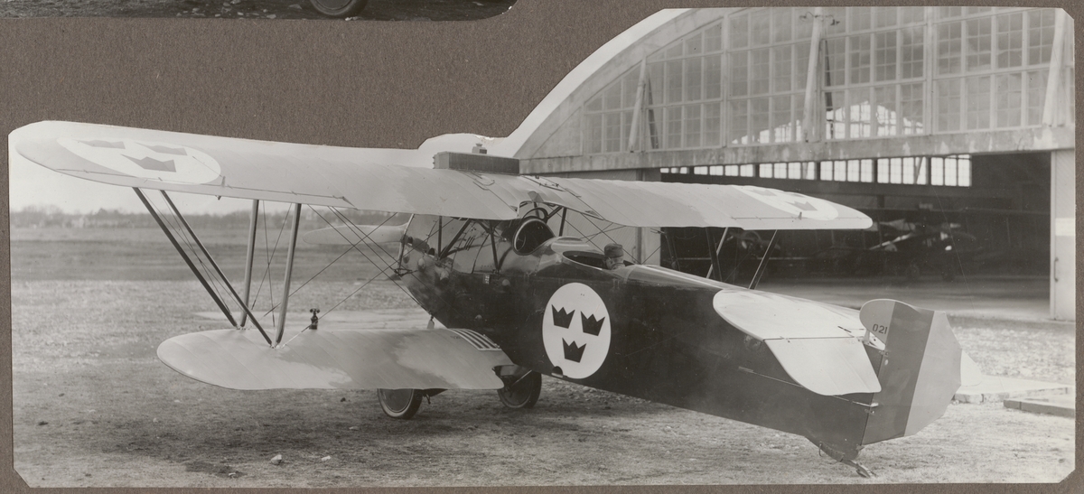 Flygplan Ö 4 FVM Phönix C.I Dront nr 021 står på flygfältet på F 5 i Ljungbyhed. Hangar i bakgrunden.