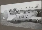 Flygplan S 6A nr 6355 står vid hangarer på ett flygfält, cirka 1932-1935. Vy bakifrån.