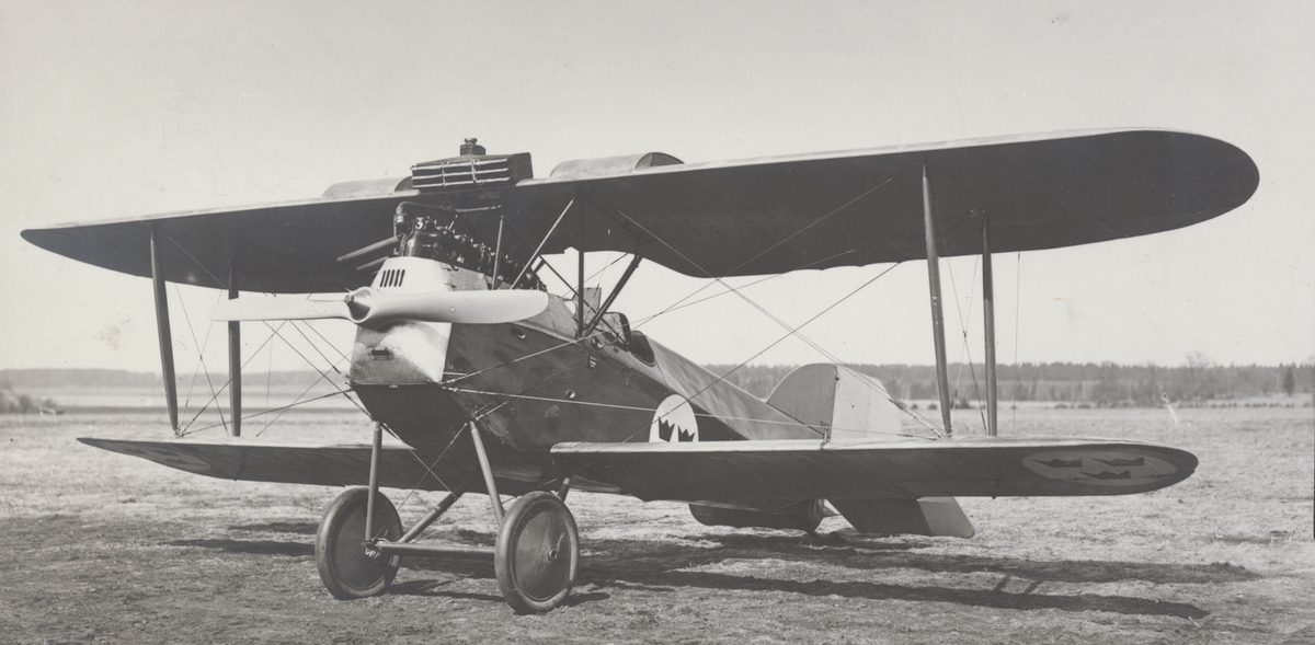 Flygplan J 1 Phönix Dront står på flygfältet på Malmen, cirka 1926-1932. Vy snett framifrån.

Text vid foto: "Phönix - J 1."