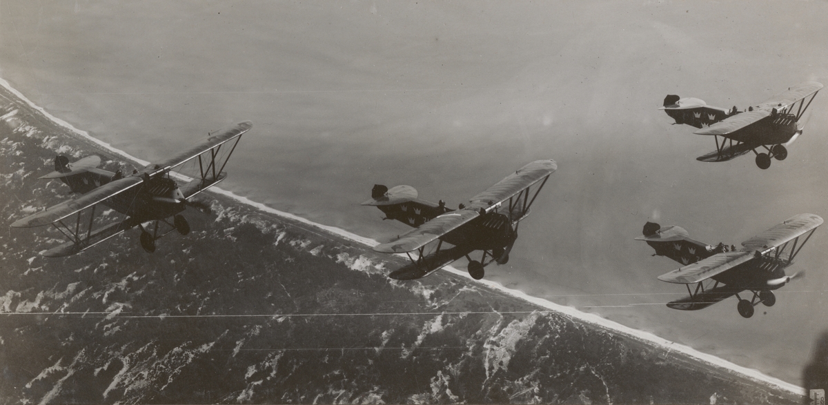 Fyra flygplan Phönix Dront flyger längs kust, 1925. Flygbild uppifrån.

Text vid foto: "Dront-patrull. 1925."