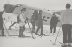 Militärer på skidor står vid ambulansflygplan Trp 2, Junkers W 34, vintertid. Flygare vid planet.