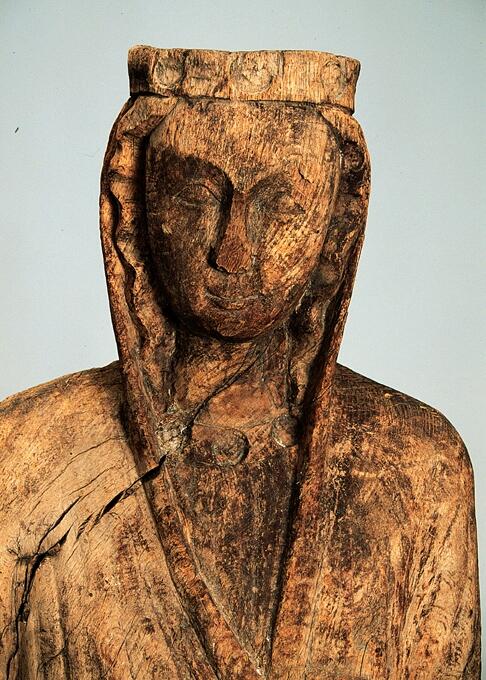 Madonna. Träskulptur. Sitter i frontal ställning å bänk. Huvudet något litet lutat mot höger. Detta har kronring med 3 ringformade fördjupningar. Från huvudet nedhänger ett kläde, som övergår i en mantel, å kroppens framsida något dragen mot höger. Barnet i fotsid dräkt sitter på vänsterknät. Barnets huvud och vissa sidodelar av bänken är borta. Polykromeringen helt och hållet förstörd. Manteln är sluten och stiger upp omkring madonnans hufvud.  Madonnans mantel bildar en V-formad halslinning, sveper tätt runt benen och på sidorna bildas en rad av små veck. Vid halsen finns tre runda fördjupningar efter en utsmyckning liknande den som har funnits på kronan. Madonnans högra hand har hållit i något som nu är borta. Det som är kvar är ett hål i den knutna handen. Madonnans hår är vågigt och syns under huvudbonaden. Näsan och en del av hakan är avslagna.