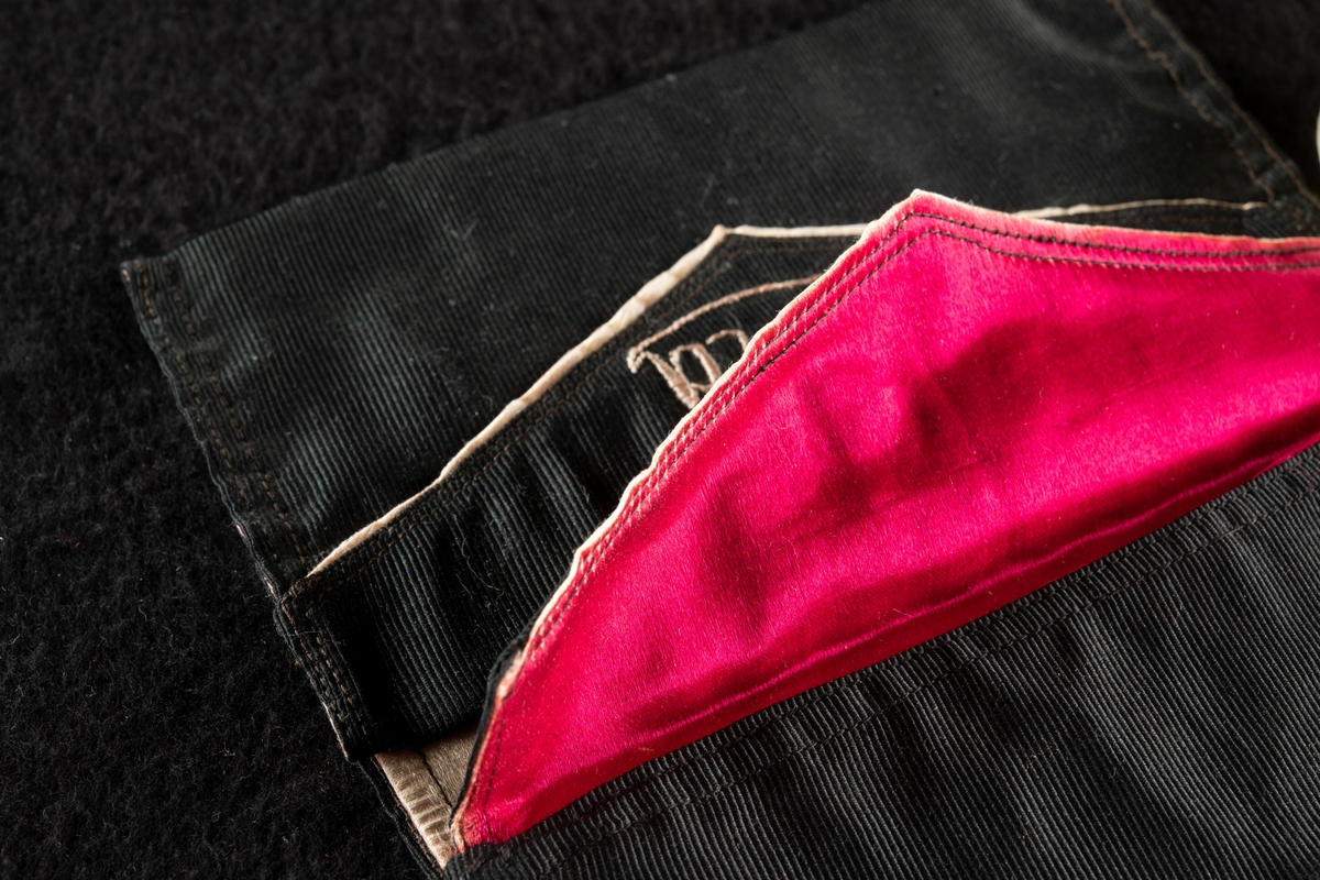 Plånbok av svart ripssiden. Invändigt klädd med rött siden. Broderad i rött med "Gösta" och "G. F." Det röda fodret samt bokstäverna har blekts betydligt och har nu en blekt gul färg.