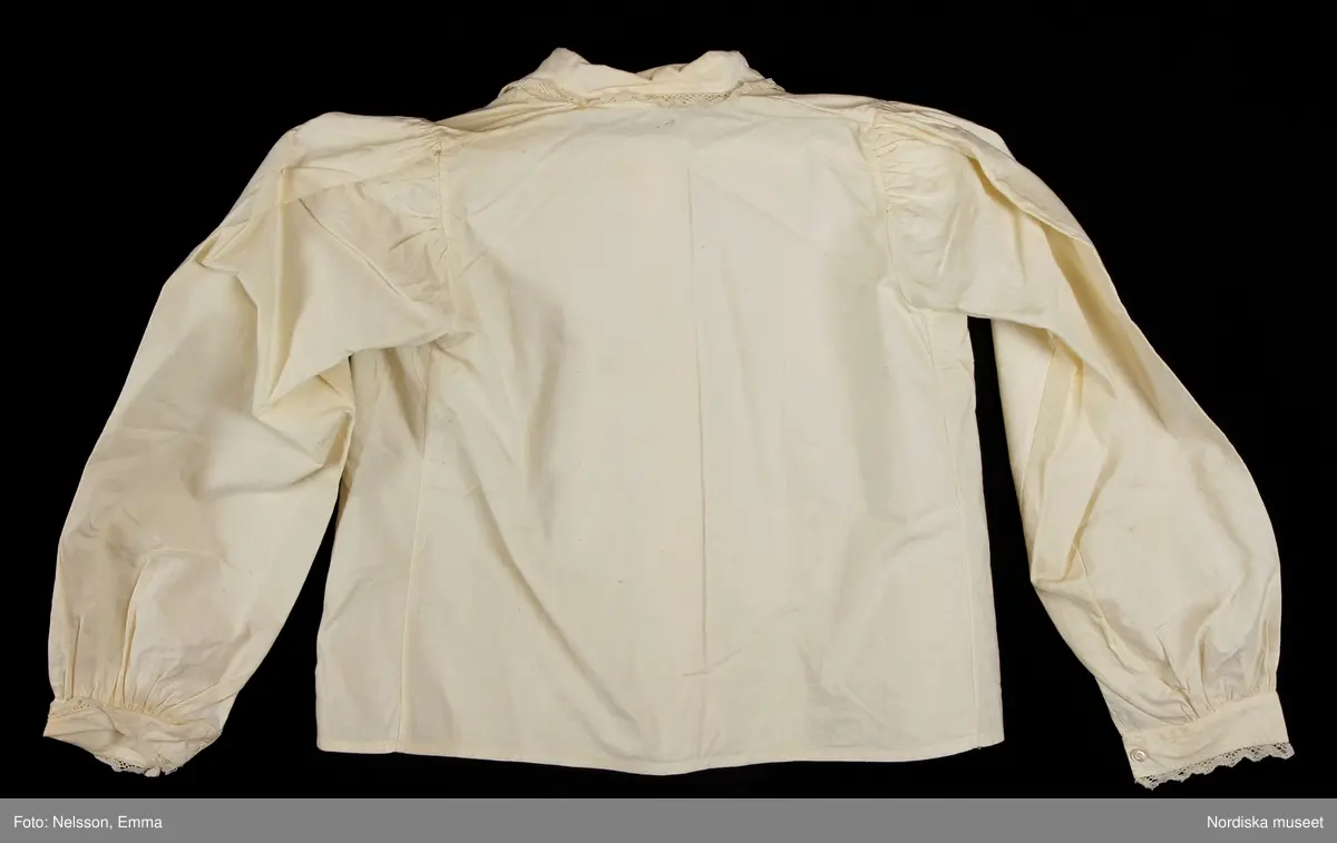 Katalogkort:
""Österåkersdräkt", 5 delar, för 8-åring. 
Bestående av överdel, livstyckekjol, förkläde, huvudbonad och bälte. 
Överdelen av vit bomullslärft med knypplad kantspets. 
Livstyckekjolen; rött kläde i kjolen, livet av gul sidenatlas med silkebroderier.
Förklädet av grön kläde med bårder nedtill i silkebroderier samt bandgarnering. Midjelinningen samt kantslå nedtill av svart kläde även dessa broderade. 
Bälte av rött läder med silkebroderier. 
Huvudbonad, best. av röda valkar, spetsluva och tyllhuckle."