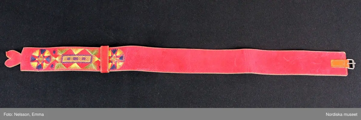 Katalogkort:
""Österåkersdräkt", 5 delar, för 8-åring. 
Bestående av överdel, livstyckekjol, förkläde, huvudbonad och bälte. 
Överdelen av vit bomullslärft med knypplad kantspets. 
Livstyckekjolen; rött kläde i kjolen, livet av gul sidenatlas med silkebroderier.
Förklädet av grön kläde med bårder nedtill i silkebroderier samt bandgarnering. Midjelinningen samt kantslå nedtill av svart kläde även dessa broderade. 
Bälte av rött läder med silkebroderier. 
Huvudbonad, best. av röda valkar, spetsluva och tyllhuckle."