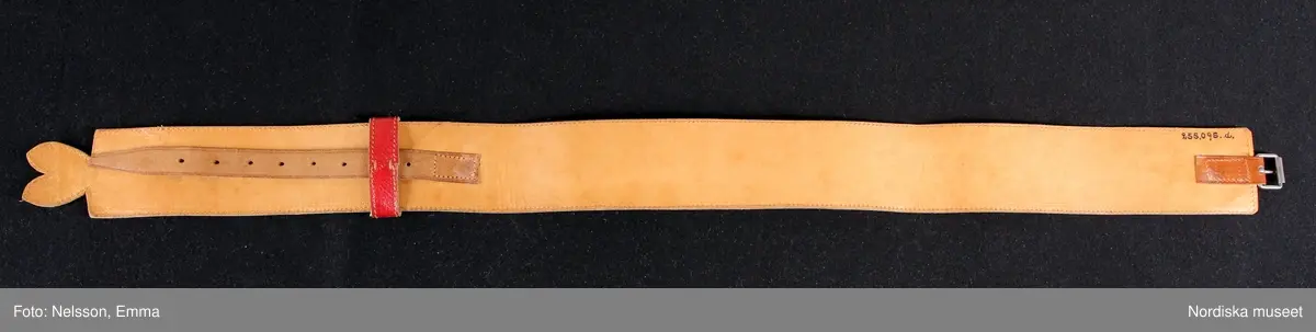 Katalogkort:
""Österåkersdräkt", 5 delar, för 8-åring. 
Bestående av överdel, livstyckekjol, förkläde, huvudbonad och bälte. 
Överdelen av vit bomullslärft med knypplad kantspets. 
Livstyckekjolen; rött kläde i kjolen, livet av gul sidenatlas med silkebroderier.
Förklädet av grön kläde med bårder nedtill i silkebroderier samt bandgarnering. Midjelinningen samt kantslå nedtill av svart kläde även dessa broderade. 
Bälte av rött läder med silkebroderier. 
Huvudbonad, best. av röda valkar, spetsluva och tyllhuckle."