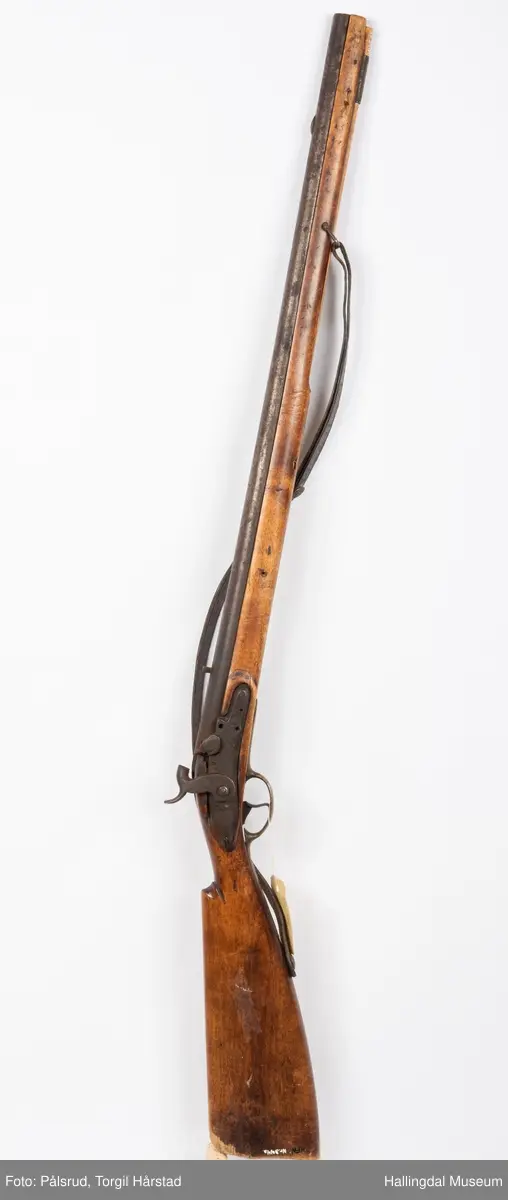 Gevær, modell fra 1769 - 1793, som er ombygd fra flintlås til perkusjonslås. Vært brukt av "Norske Gevorbne Jeger Corps" og senere av soldat nr. 90 i "Telemarkske Nationale jeger Corps Westenfjeldske Compani" i perioden 1818 - 1839. Geværet mangler kolbekappe, men har antatt original reim i brunt lær med messingknapp. Ladestokk i tre.