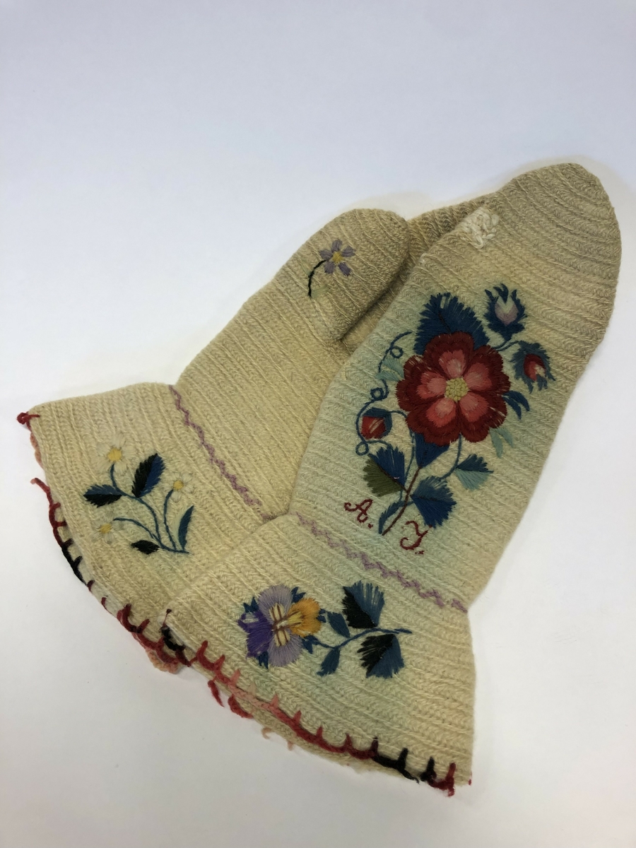 Broderte ullvotter med initialer A.J. og blomstermotiv.