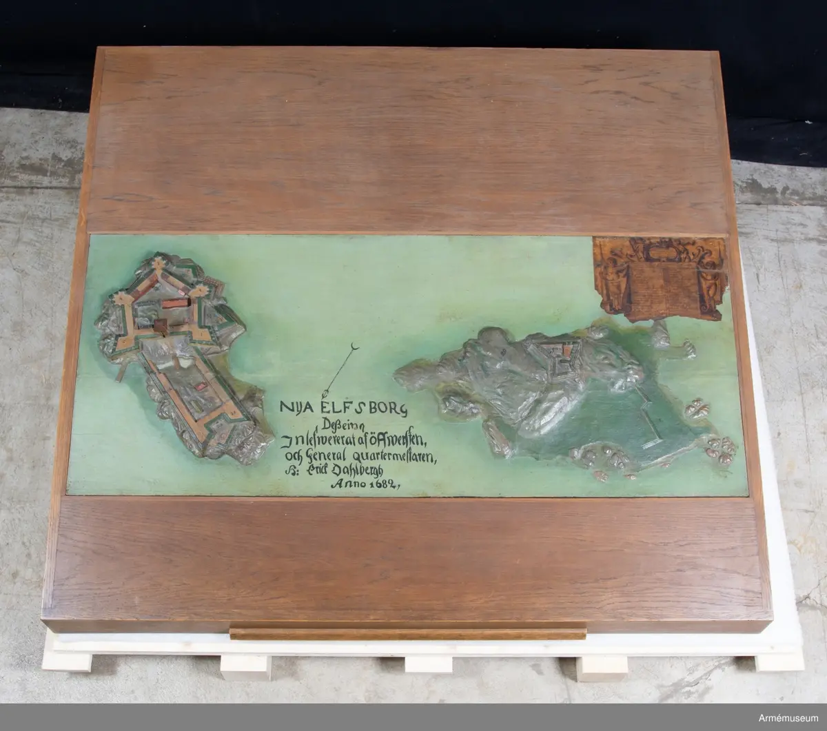 Modellen har påskrift: "Nya Elfsborg Desseing inlefwererat af Öffwersten och General quartermestaren h: Erich Dahlbergh anno 1682".

Modellen är 565x1355 mm och utförd av två ekbrädor med en ursprunglig tjocklek av 50 mm. Holmarna är skurna direkt ur plattan, som vid vattnet har sin minsta tjocklek av 25 mm. Även själva befästningarna är skurna i ett med plattan, endast husen och tornet är skurna för sig och fastsatta. I övre högra hörnet sitter en påklistrad lapp med förklaringar. I inventariet 1768 hade modellen nr 2, men siffran finns inte längre kvar. 
Förmodligen vid renoveringen på 1880-talet har man skrivit av texten, som sedan av misstag hamnat på baksidan av Bohus fästning. 1939 rengjordes modellen från fernissa och smuts, flagnande färg fästes och modellen mattfernissades.

Texten omges av voluter och putti med slöjor och smala pyramider, överst en kartusch med två putti. "Delination af Nya Elfsborg och des uthanwärck med Assp-holmen afmätit
och förfärdigat anno 1678 d. 1 november."

"Explication öfwer Bastionerne sampt andre notable orthers nampn".
1. Hummeren
2. Hwalfisken
3. Haffrunn
4. Delfin
5. Norrstiärnan
6. Porttornet
7. Catsamatan hwar uthi dhen öfwerste håller predikan för guarnizon
8. Commendantens logumente
9. Under Commendantens logumente
10. Prästens och Condeutörens logumenter
11. Lieutnampters och Fändrichers logumenter
12. Constabler och handtlangare
13. Wachtmästarens logumente
14. Archliemästarens
15. Wacht Corps de Guarde
16. Sortier eller löönportar
17. Brunn och friskt watn
18. Ravalinen
19. Hornwärcket
20. Baracquen
21. Kalekboden
22. Uthi hornwärcket sortier
23. Norr Horn
24. Wäster Horn
25. af master ophugne ravalin
26. Hamn för båthar
27. Tvänne Brunnar med färskt watn
28. Bryggian hwarest farkoster anläggia
29. Asspholmen
30. dhet dher nyss upparbetadhe Tenaliewärcket
31. Ett opkastat Trensiement emot watenet

Nederdelen av texten är borta där förmodligen David Lydings signatur stått.