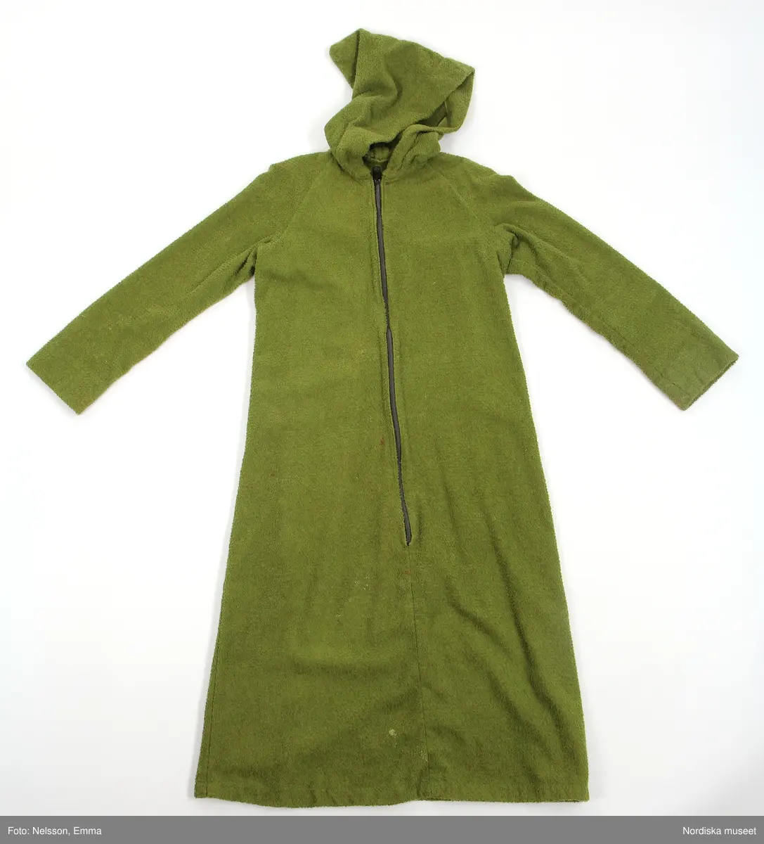Katalogkort:
"Morgonrock av grön frotté. Utställd modell med huva och långa ärmar. Dragkedja från halslinning till 36 cm från fåll."