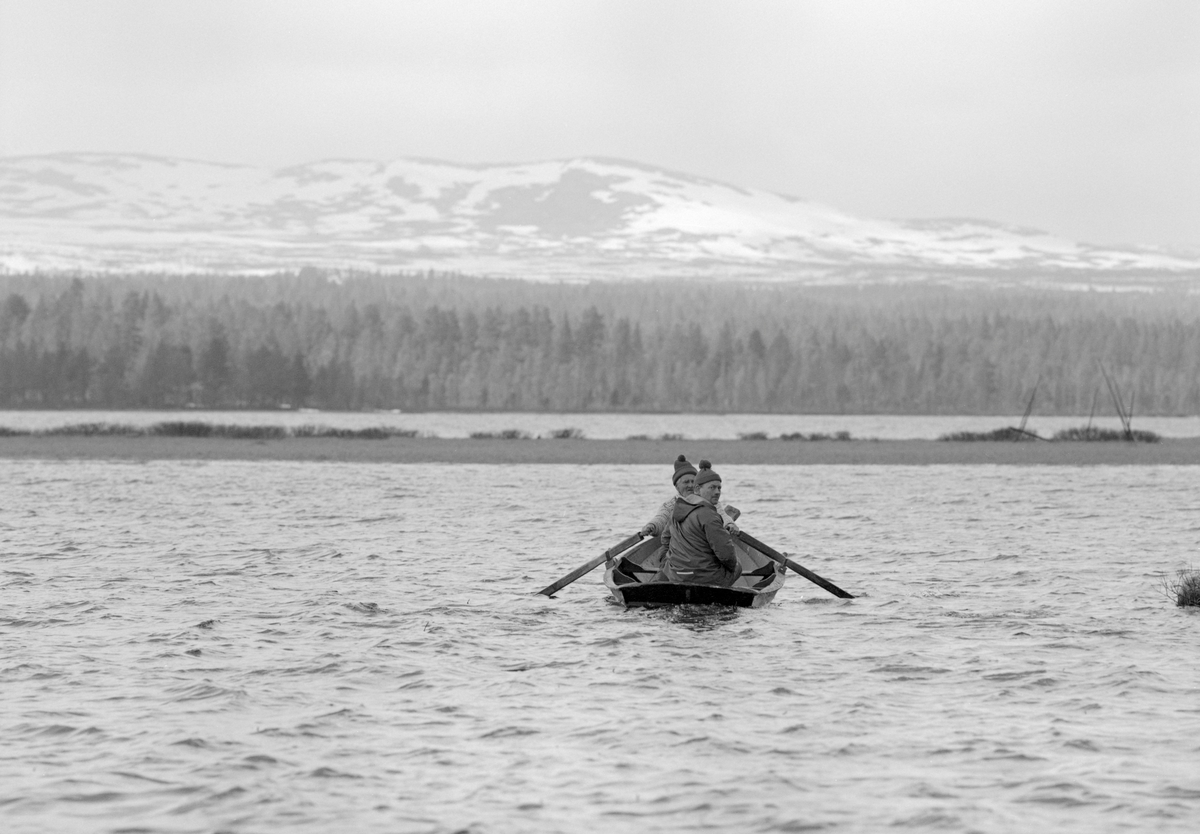 Gjeddefiske i deltaområdet der elva Tufsinga renner ut i innsjøen Femund. Lokaliteten ligger i Tufsingdalen i Os kommune i Nord-Østerdalen, bortimot 700 meter over havet. Fotografiet viser to menn i en klinkbygd trebåt med tverr akterende. Karene skulle trekke gjeddegarn. Vi vet foreløpig ikke hvem mannen i akterenden av båten var. Han som satt ved årene var «gjeddekongen» Joseph Bakken (1898-1989). Gjeddefisket i dette området foregikk i mai måned, like etter at isen på vassdragene hadde smeltet. Da trakk gjedda inn mot de sivbevokste grunnene langs land for å gyte. Der satte fiskerne garn skrått ut fra strandlinja. Det var slike garn de to mennene i båten skulle sette eller trekke da dette fotografiet ble tatt.