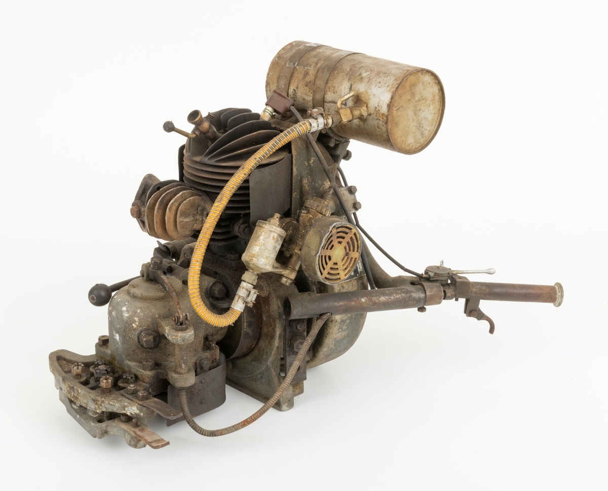 Motor til en tomanns motorsag fra den tyske Dolmar-fabrikken, sverdet og eksospotta (antatt ekspospotte, se SJF.14799) til saga mangler. Saga har to håndtak bak motoren. Det sitter en tennplugg på toppen av motoren.