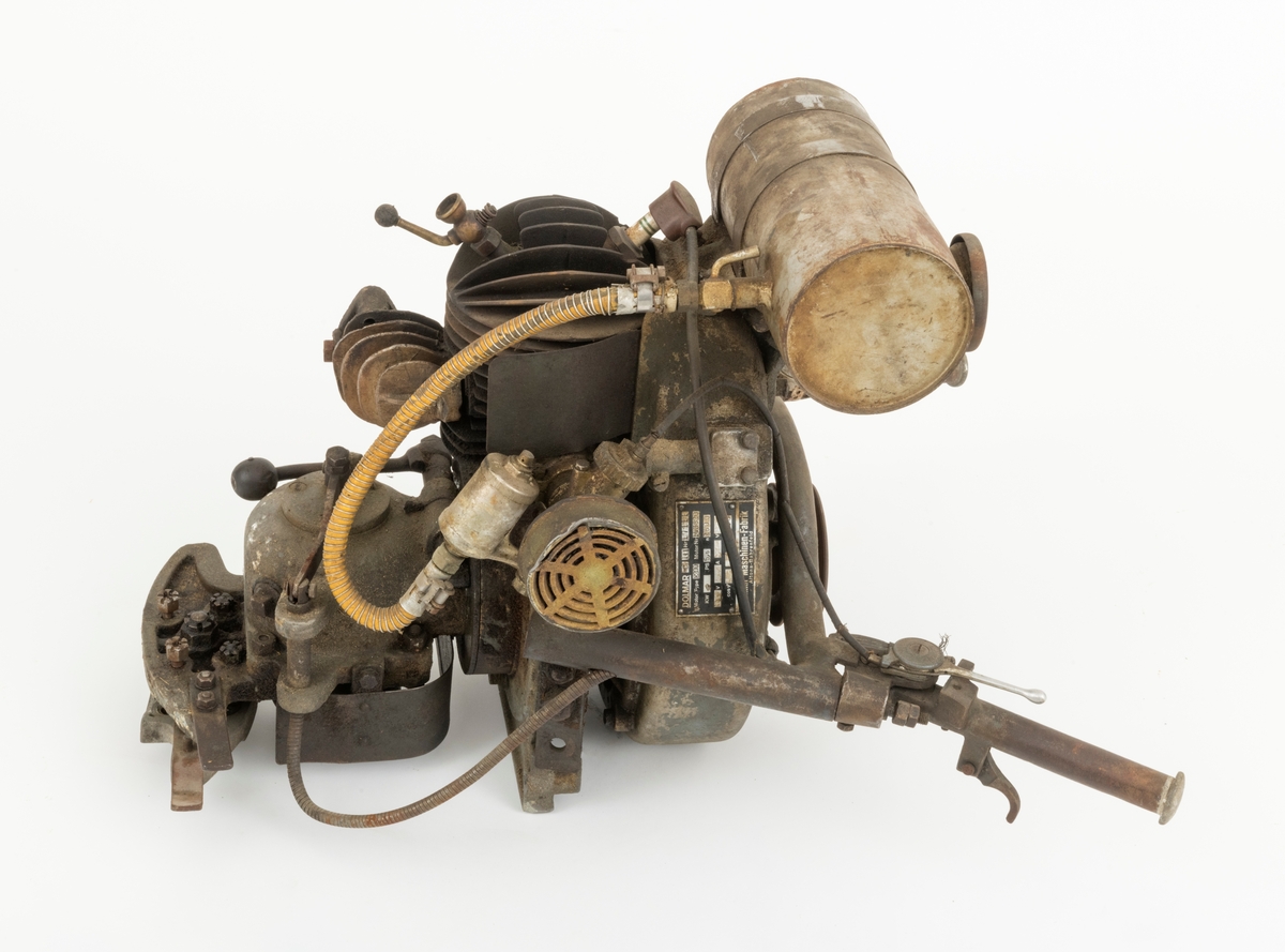 Motor til en tomanns motorsag fra den tyske Dolmar-fabrikken, sverdet og eksospotta (antatt ekspospotte, se SJF.14799) til saga mangler. Saga har to håndtak bak motoren. Det sitter en tennplugg på toppen av motoren.