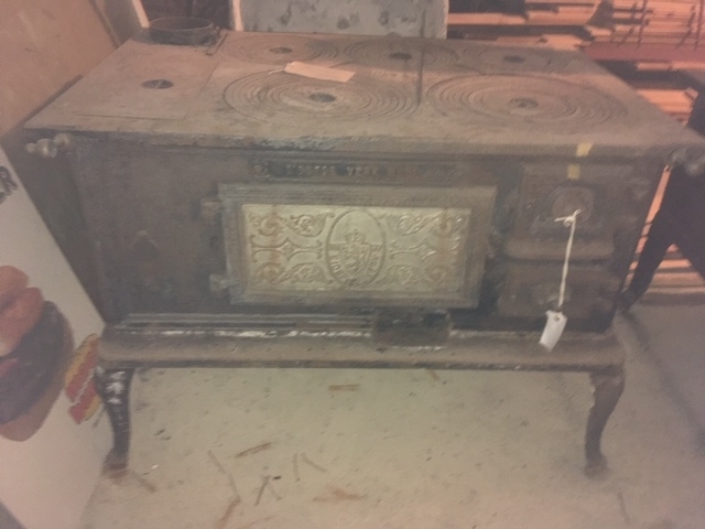 Komfyr i støpejern med venstrehengslet ileggsdør til venstre og to luker til høyre, fem plater med ringer på toppen. Står på fire svungne ben. Dør med norske løve og planteornamentikk. Tilhørende løs messingstang til front, askekrok av jern,  ringkrok av jern og blåmalt rektangulær vedkasse av tre.