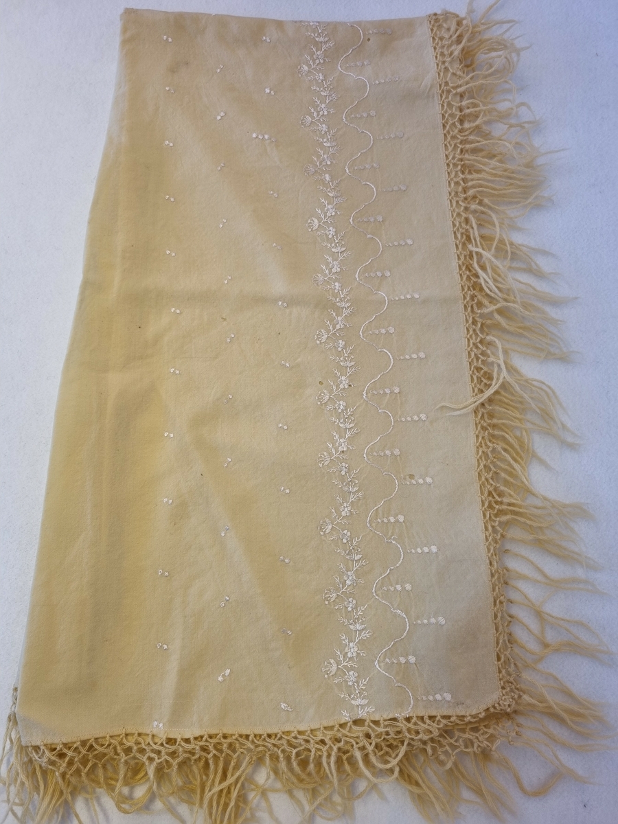Ull kypert, gulhvit.
Frynser rundt kanten.
Blomsterbord brodert med hvit silketråd langs en langside.
Reparert og sydd sammen på midten.