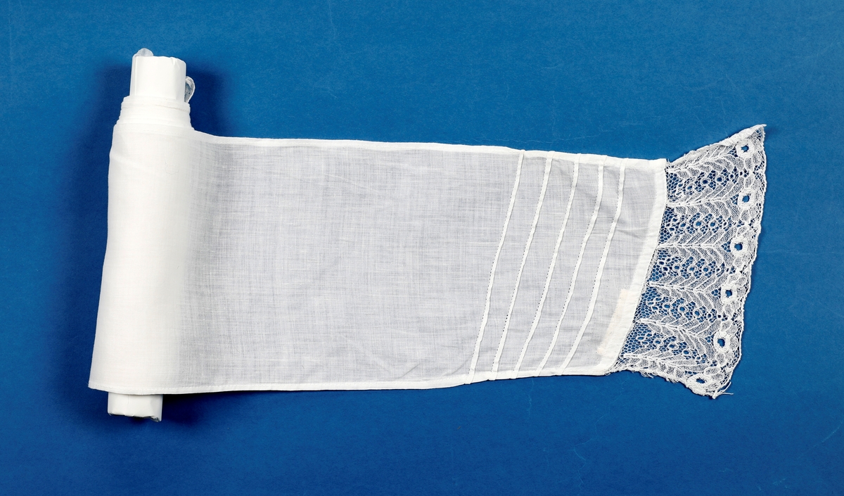 Lang dåpskjole med belte og underskjørt.
Kjolen har bærestykke hvor selve kjolen r rynket til. Halsringing, mansjetter og nedkant av skjørtet er besatt med blonder. Løpegang i halsen med knyting bak. Løpegang med knytesnor nederst på ermene. Splitt bak med to punkter med knytebånd. Forsiden av skjørtet er pyntet med biser og blonder.
Beltet er bredt, pyntet med biser og blonder i endene.
Underskjørtet har løpegang i livet og påsydd kappe i engelsk blonde.