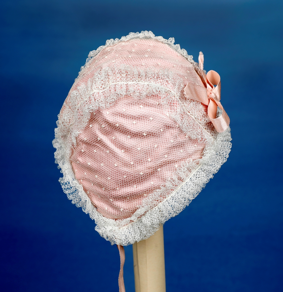 Dåpskjole med tilbehør: belte, lue, votter.  

Dåpskjole med isydde ermer, skulderstykke, langt vidt skjørt med rynker. Dekorteknikk: Foldelagte kapper 2 foran, 1 bak festet med blonde. Sydde legg, 5 stk., festet med blonde. Åpning bak 40 cm med 2 knytteband. pyntet med rosa bånd.
Lue:bobinet foret med rosa sateng. 
belte: bredt og langt med pynt av blonder og biser i hver ende.
Strikkede votter, tradisjonell form med knyttesnor.