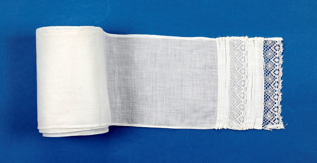 Dåpskjole med tilbehør: belte, lue, votter.  

Dåpskjole med isydde ermer, skulderstykke, langt vidt skjørt med rynker. Dekorteknikk: Foldelagte kapper 2 foran, 1 bak festet med blonde. Sydde legg, 5 stk., festet med blonde. Åpning bak 40 cm med 2 knytteband. pyntet med rosa bånd.
Lue:bobinet foret med rosa sateng. 
belte: bredt og langt med pynt av blonder og biser i hver ende.
Strikkede votter, tradisjonell form med knyttesnor.