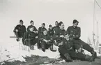 Tio flygsoldater sitter på marken under rast i Kiruna, vintertid, april 1942.

Bildtext vid foto: 