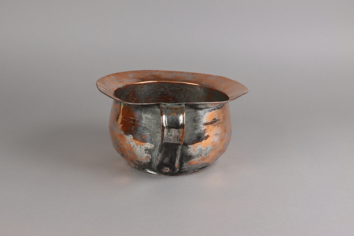 Copper chamber pot, plain circle form with flat base, angled rim above domed base with s-scroll handle. The pot shows traces of tin lining in the pot, on the handle and on the sides.