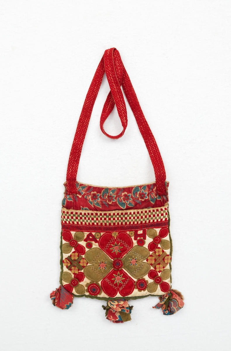 Kjolsäck, liduväska, till Boda sockendräkt för kvinna. Av vitt skinn med applikationer i grönt, gult och rött ylletyg, hjärtformer och blad. Broderier av silke och bomullsgarn i form av stjärnor och flätsömmar. På framstyckets överkant flätad dekor av smala skinn och tygremsor. Vid nederkanten små tofsar av tygbitar av olika kvaliteter. Passpoal av grönt ylletyg runt kanterna. Fickspegel av rödbottnad kattun. Baksida av vitt rakat skinn. Foder av kypertvävt linnetyg. Överkant på ficka och bakstycke kantat av vitt skinn. Vid överkantens hörn fastsytt ett mönstervävt band av rött ullgarn på vit botten. Märkning med initialer av rött ylletyg på framsidan: A H