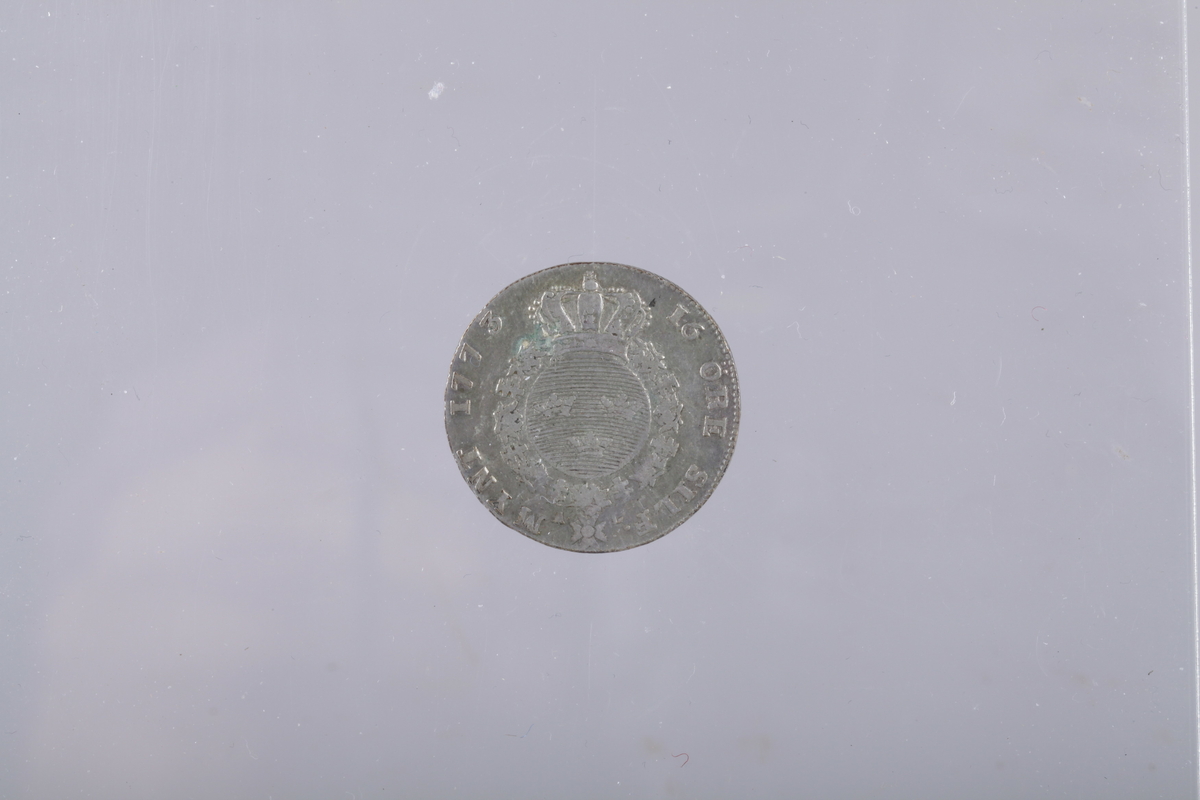 Svensk 16 øre 1773, Forsiden: Stor G (Gustav III) med romertallet III inni og kongekrone oppå,  Rest av opphøyet kant med små rifler innenfor. baksiden: sirkelrundt bueformet våpenskjold med 3 kroner, kongekrone på toppen, rundt skjoldet ordenskjede med stjerneformet ordenssymbol. rest av opphøyet kant med små rifler innenfor.
