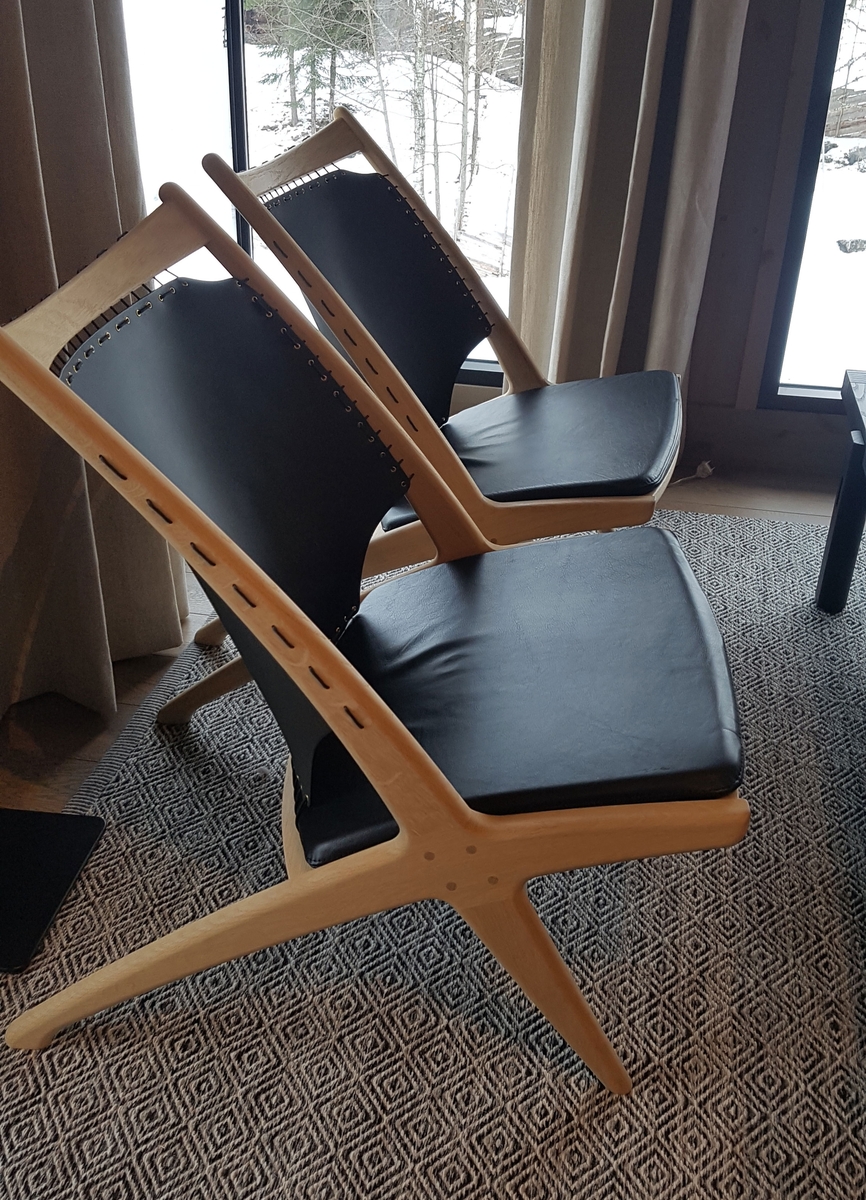 Lenestol av tre med svart skinn som er strukket som et segl i ryggstøtten. Svart sittepute av skinn. Stolbeina og ryggstøtten er formet som et kryss.