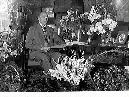 Carl Bartholdsson, en av cheferna på Monark, fyller 50 år. Han sitter bland sina gratulationsbuketter och på bordet även en Odd Fellow-flagga.