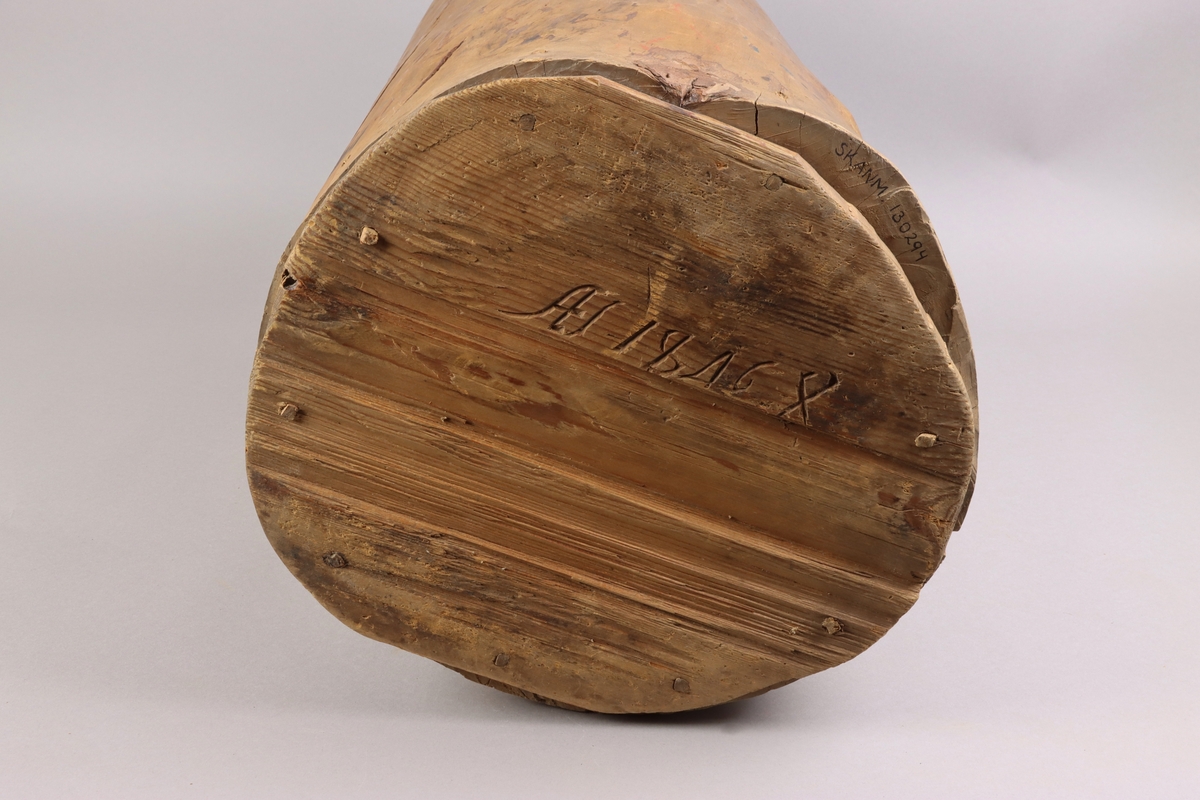 A wooden barrel, carved from the trunk of the tree, below a flat cylindrical end attached with dowels up on the sides of the vessel.