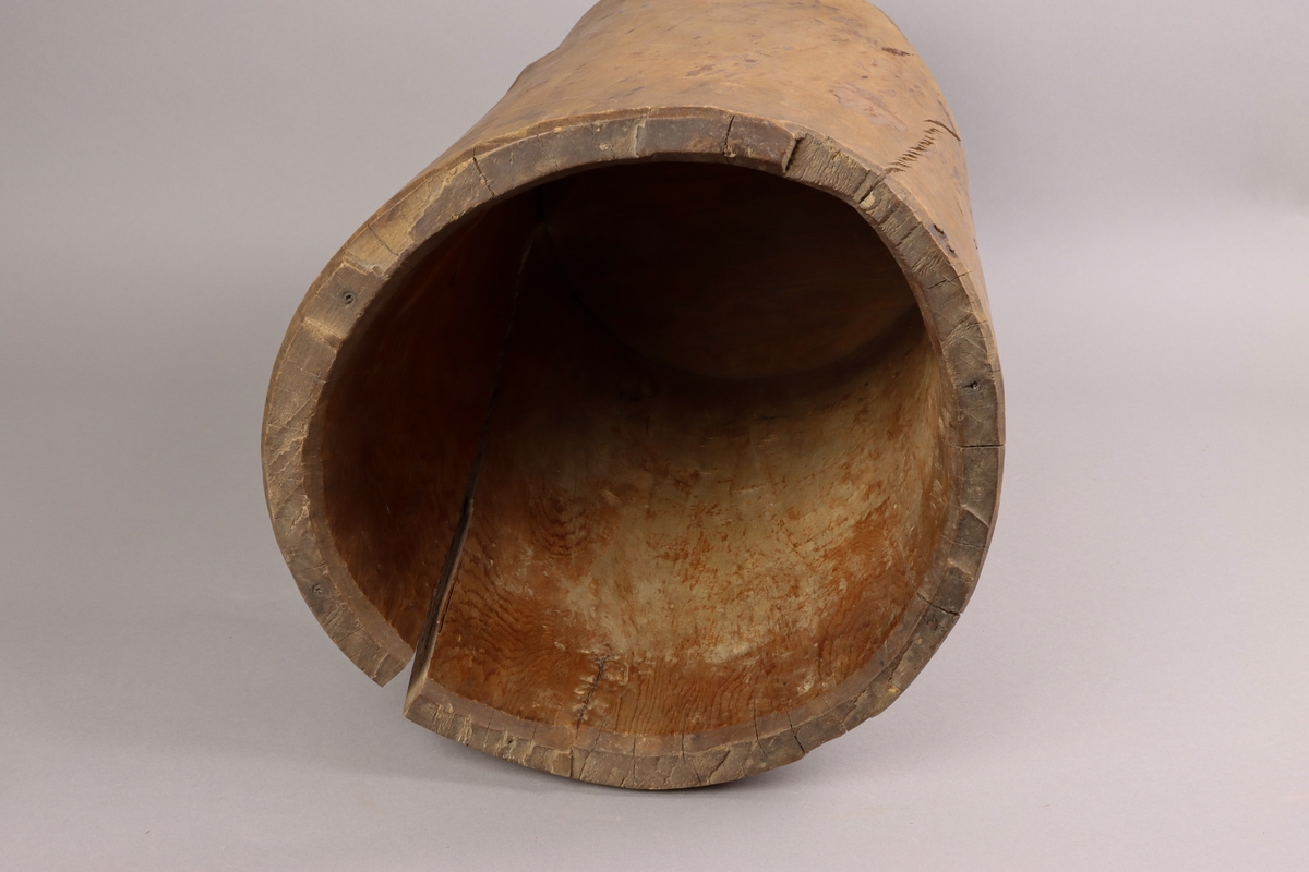 A wooden barrel, carved from the trunk of the tree, below a flat cylindrical end attached with dowels up on the sides of the vessel.