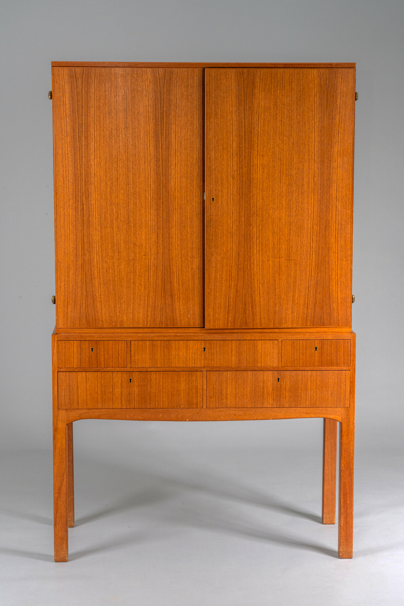 Skap på høye bein. To skapdører, en rekke med 3 skuffer og en rekke med 2 skuffer under, alle låsbare. Har tilhørt Sara Fabricius.