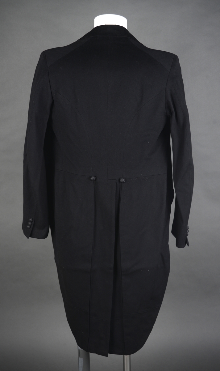 Snippkjole med vest.
Snippkjole i svart ullstoff med slag sydd av satengvevd silkestoff. 1 knapphull på venstre slag. Bakovertrekte skulder- og sidesømmer. 1 innerlomme på høyre framstykke og 1 på venstre. 1 innsnitt og 3 trekte knapper på hver framstykke. Splitt fra livet og ned MB. Dekor 2 trekte knapper i livet ved splitten. Wienersømmer i ryggen og søm MB. Plagget er avtatt i livet. Tosømsermer med lukket splitt med 3 trekte knapper. Plagget har innsydde skulderputer og er helforet. Hempe og firmamerke i nakken. Firmamerke inne i innerlommen på høyre framstykke.
Vest i svart ullstoff på forstykket og satengvevd blankt stoff på ryggen. Spensel med spenne på ryggen, søm MB med en splitt i nedre kant. Vesten er dypt halsrigning og har påsydd et hvitt dekorbånd langs rigningen. Lukkes med 4 trekte knapper. 2 lommer foran. Vesten er foret med hvitt bomullsfor med svarte striper. Samme for som i ermene på snippkjolen. Vesten er antakelig utsydd i sidene en gang.