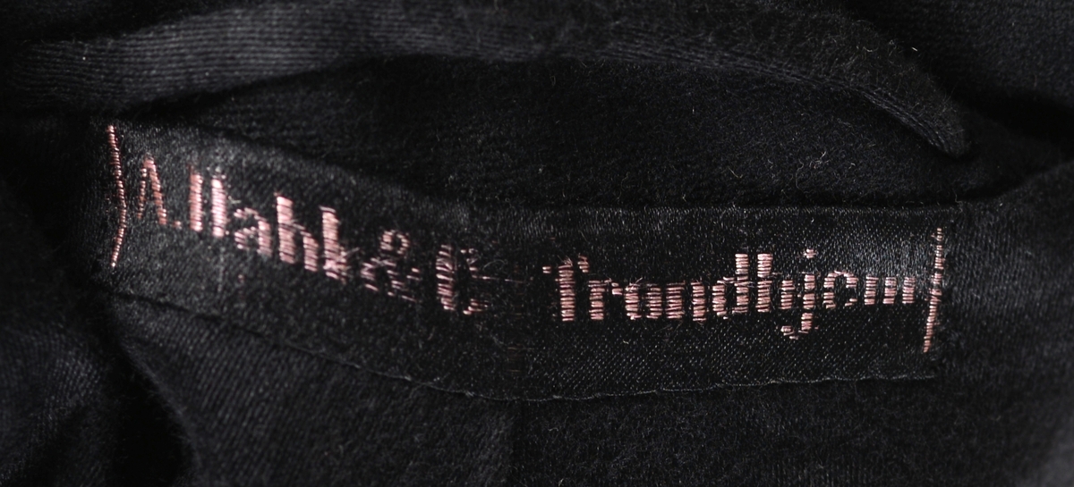 Snippkjole med vest.
Snippkjole i svart ullstoff med slag sydd av satengvevd silkestoff. 1 knapphull på venstre slag. Bakovertrekte skulder- og sidesømmer. 1 innerlomme på høyre framstykke og 1 på venstre. 1 innsnitt og 3 trekte knapper på hver framstykke. Splitt fra livet og ned MB. Dekor 2 trekte knapper i livet ved splitten. Wienersømmer i ryggen og søm MB. Plagget er avtatt i livet. Tosømsermer med lukket splitt med 3 trekte knapper. Plagget har innsydde skulderputer og er helforet. Hempe og firmamerke i nakken. Firmamerke inne i innerlommen på høyre framstykke.
Vest i svart ullstoff på forstykket og satengvevd blankt stoff på ryggen. Spensel med spenne på ryggen, søm MB med en splitt i nedre kant. Vesten er dypt halsrigning og har påsydd et hvitt dekorbånd langs rigningen. Lukkes med 4 trekte knapper. 2 lommer foran. Vesten er foret med hvitt bomullsfor med svarte striper. Samme for som i ermene på snippkjolen. Vesten er antakelig utsydd i sidene en gang.