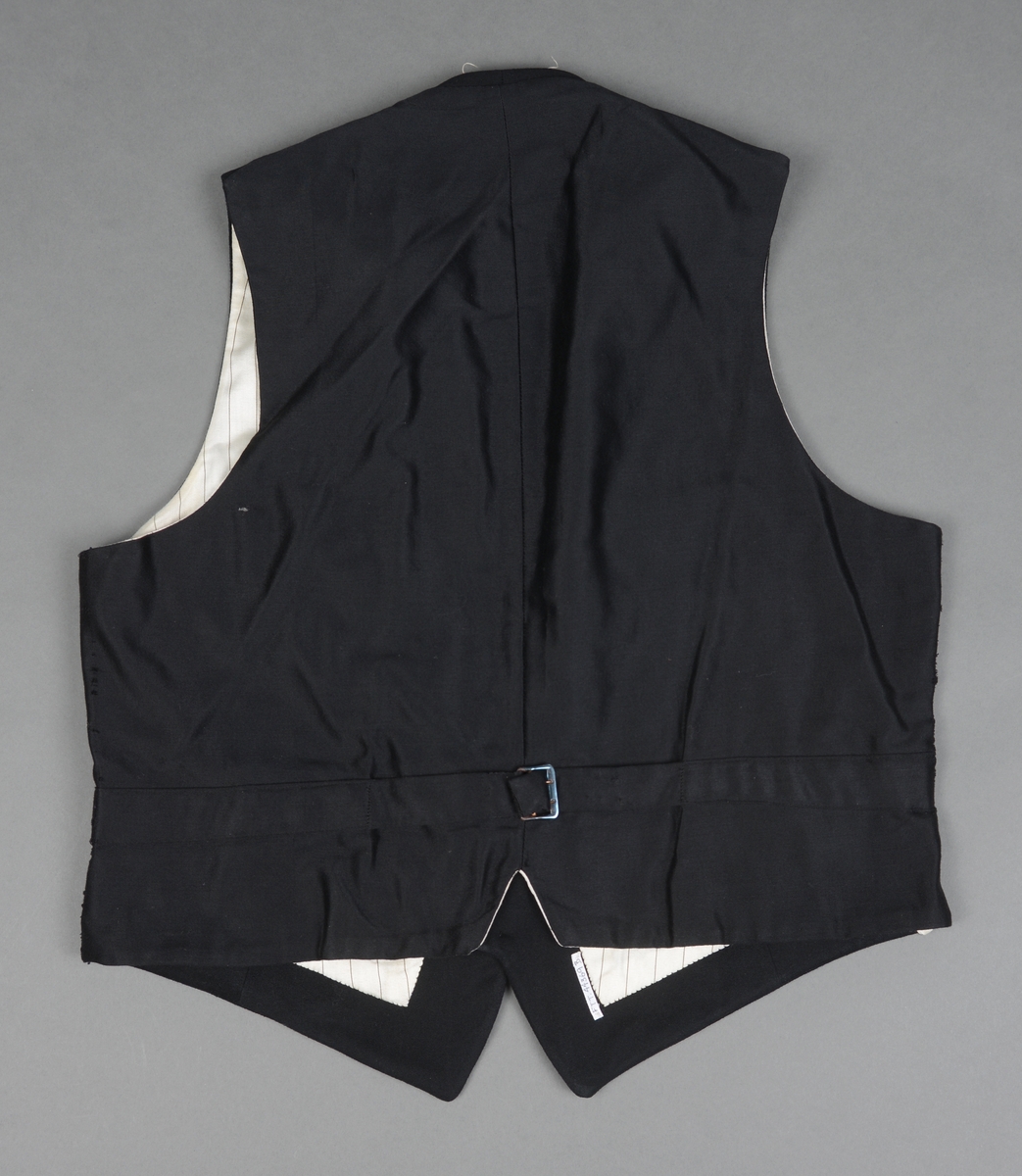 Snippkjole med vest.
Snippkjole i svart ullstoff med slag sydd av satengvevd silkestoff. 1 knapphull på venstre slag. Bakovertrekte skulder- og sidesømmer. 1 innerlomme på høyre framstykke og 1 på venstre. 1 innsnitt og 3 trekte knapper på hver framstykke. Splitt fra livet og ned MB. Dekor 2 trekte knapper i livet ved splitten. Wienersømmer i ryggen og søm MB. Plagget er avtatt i livet. Tosømsermer med lukket splitt med 3 trekte knapper. Plagget har innsydde skulderputer og er helforet. Hempe og firmamerke i nakken. Firmamerke inne i innerlommen på høyre framstykke.
Vest i svart ullstoff på forstykket og satengvevd blankt stoff på ryggen. Spensel med spenne på ryggen, søm MB med en splitt i nedre kant. Vesten er dypt halsrigning og har påsydd et hvitt dekorbånd langs rigningen. Lukkes med 4 trekte knapper. 2 lommer foran. Vesten er foret med hvitt bomullsfor med svarte striper. Samme for som i ermene på snippkjolen. Vesten er antakelig utsydd i sidene en gang.