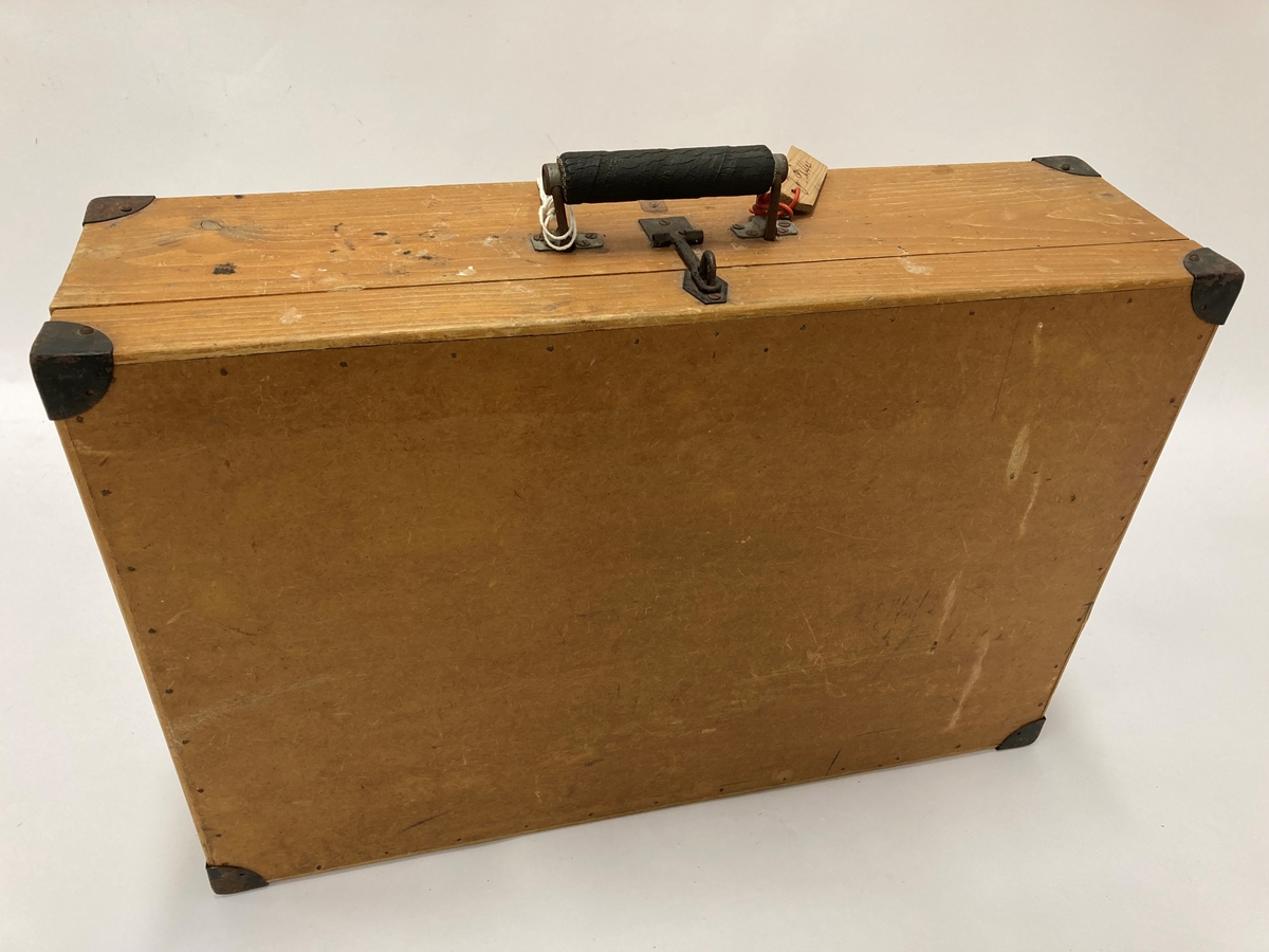 Trekoffert med hengslet lokk. Laget av plater, planker og lister. Metallbeslag i hjørnene. Håndtak på langsiden med vedheftet treskilt merket "8218" på fremsiden og på baksiden J. Østlie. Papiretikett på kortsiden "Halden 183". Kassen inneholder fangedrakten til Johan Østlie, Kornsjø, brukt i Grini fangeleir.