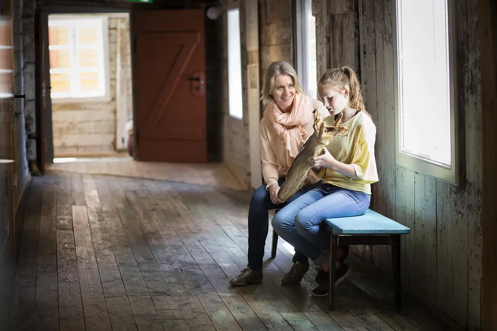 Mor og datter sitter på benk i svalgangen og studerer en tørrfisk