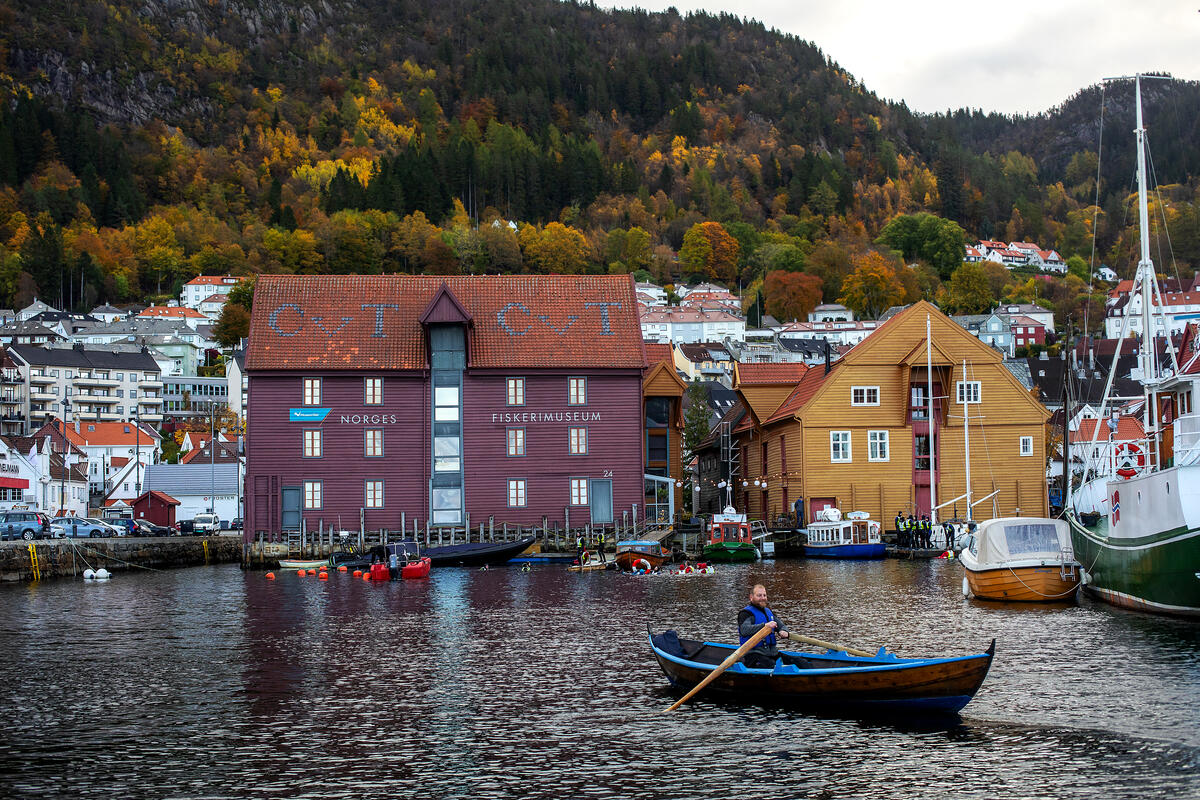 Havnen foran Norges Fiskerimuseum en fin høstdag, og en mann i robåt ror i forgrunnen
