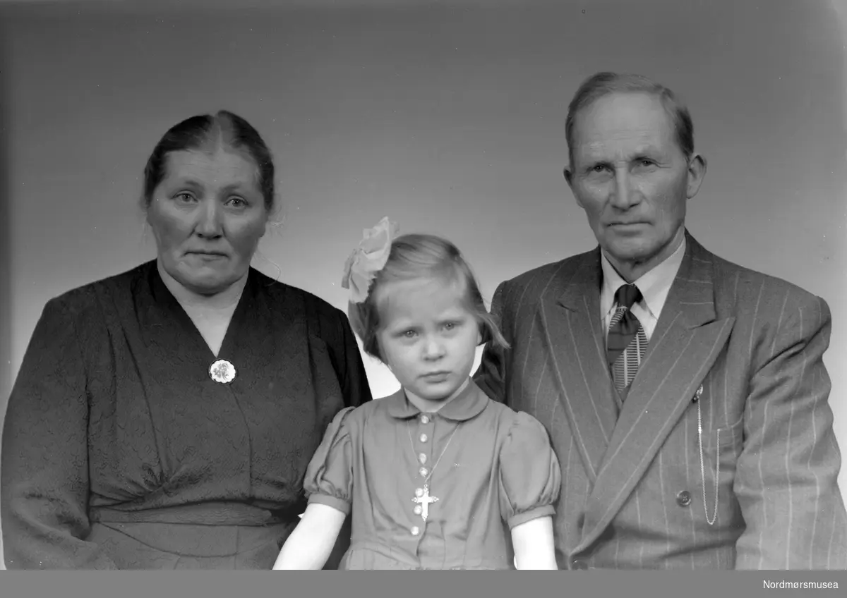 Liten pike med sine besteforeldre. Bildet er registrert på navnet Skjærseth. Fra fotoarkivet etter portrettfotograf Claus Monge. Nordmøre museum overtok samlingen fra sommeren 2011.