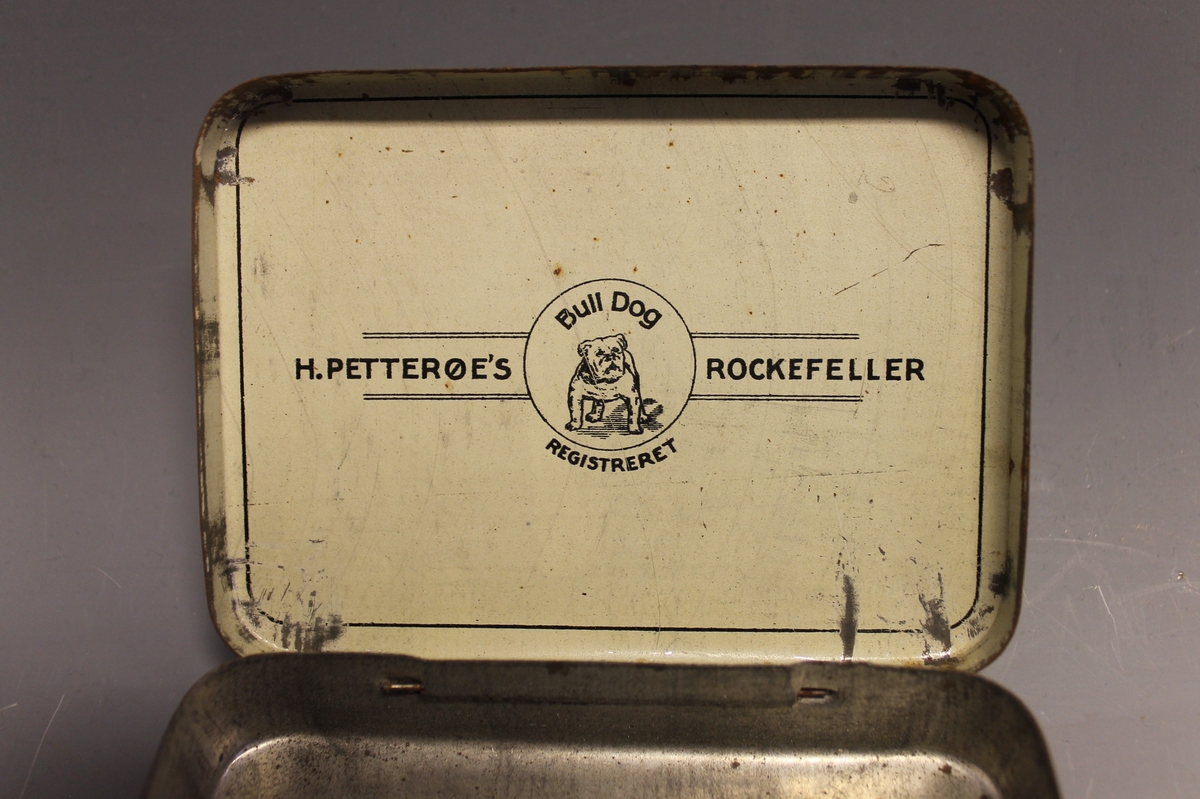 På lokket: AMERICAN GRANULATED PLUD TOBACCO ROCKEFELLER H: PETTERØE KRISTIANIA, inni lokket: H. PETTERØES ROCKEFELLER Bull Dog REGISTRERET, tegning av bulldog
