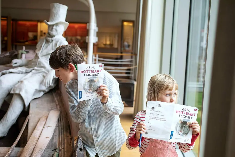 To barn som holder opp en brosjyre hver som sier "Gå på Rottejakt på museet"