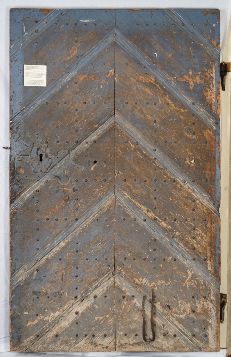 Døra består av tre planker på innsida, satt sammen med dragspon, som senere er høvla ned så døra er helt plan. Har jernbeslag på innsida, over dragspon, som fungerer som hengsler. 

Jernbeslag midt på døra på innsida, med bokstavene "OOS" og "BTS".

Jernlås festa med jernspiker. Nøkkelhullbeslag i jern. 

På utsida kledd med profilerte bord med not og fjær. Festa med jernnagler. 

Blåmalt på framsida. Ellers umalt. 

På begge sider spor der lås har vært innfelt. På innsida er dette fylt igjen med et trestykke.