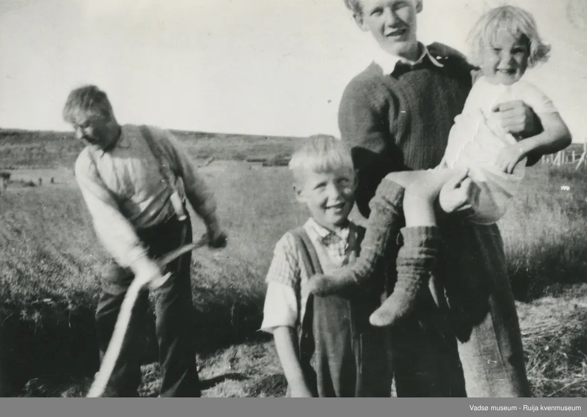 Karl Benjamin Sirkka slår høyet med ljå. Erling Stålsett løfter Anne Line Sirkka,  Karl Willhelm Sirkka står ved siden av. Bildet er fra Sikkajordet på 1950- tallet.