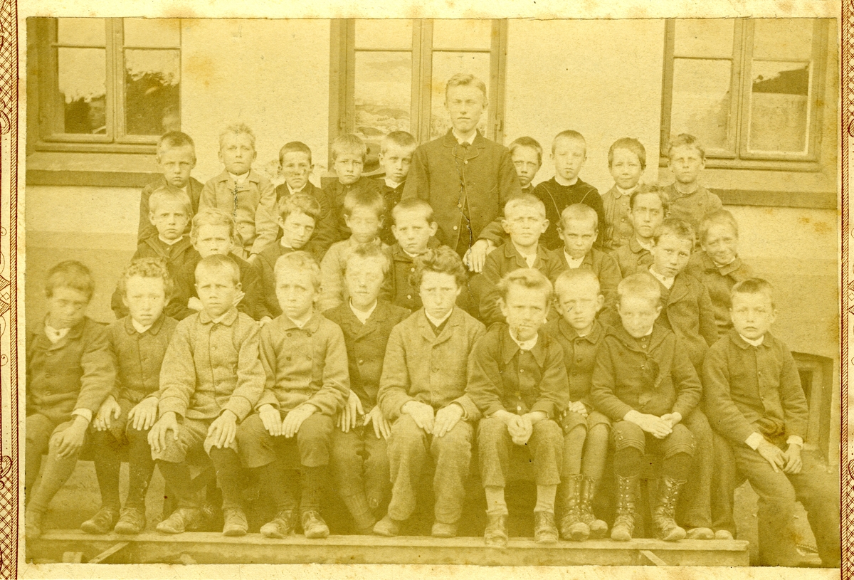 Fredrikstad. Middelskoleelever. Skolebilde. Fredrikstad høyere almenskole. (Den Gule anstalt). Gutteklasse. - Oppgitte navn:  8-åttende gutt fra venstre i andre rekke: Sigurd Helland (1875-1966), Bak ham Carsten Jacobsen (1875-1961). - Tidfesting: guttene vi kjenner navnet på er begge født i 1875. De var trolig rundt 10 år gamle da bildet ble tatt. - Klasseliste for elevene i 1884/1885: Oskar Lund, Vilhelm Støren, Markus Hannestad, Albert Olsen, Niels Smith, Arnold Arnesen, Hans Andresen, Erling Sande, Hans Robert Hansen, Mens Hansen, Carsten Jacobsen, Daniel Joohannesen, Peder Johannesen, Ivar Lanlum, Christoffer Munthe, Niels Mathisen, Ole Normann, Frits Olsen, Severin Olsen (senere etternavn Sverre), Matin Olsen, Thomas Pettersen, Jon Simonsen, Emil Syversen, Harald Sørensen, Hakon Østberg, Hans Gude Øvergaard, Kristian Kajus Ulveng, Karl Johan Schulz (el. Schultz), Johan Hjalmar Nordengen, Alexander Hanasen, Einar Johnsen, Hans Blom Sandberg, Karl Ludvig Smith. - lærer Rangsæter. - Elevenes navn er satt i tilfeldig rekkefølge.