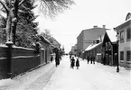 Parti av Nygatan i Linköping år 1903. Fotograf Essen hade för motivet ställt sig ett 50-tal meter före gatans skärning med Apotekaregatan i höjd med Nisbethska gården, vars höga plank löper till vänster. Vid tiden sträckte sig gårdens tomt ännu mellan Läroverksgatan och Apotekaregatan men detta kom att ändras när en stor hyresfastighet uppfördes i det synliga hörnet 1906. Förändringen i gatubilden är på det hela taget total. Samtliga byggnader är idag rivna eller i något fall flyttad till friluftsmuseet Gamla Linköping.